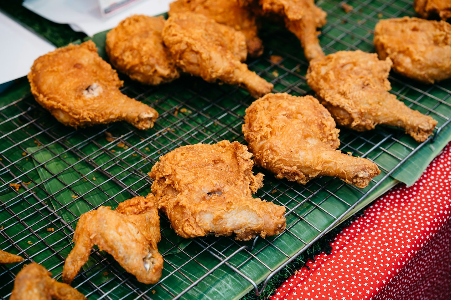 Trozos de pollo frito descansan sobre una rejilla metálica con hojas de plátano debajo.